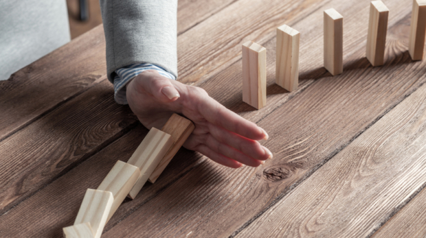 Businesswoman,Protecting,Dominoes,From,Falling,On,Wooden,Desk.,Business,Assistance